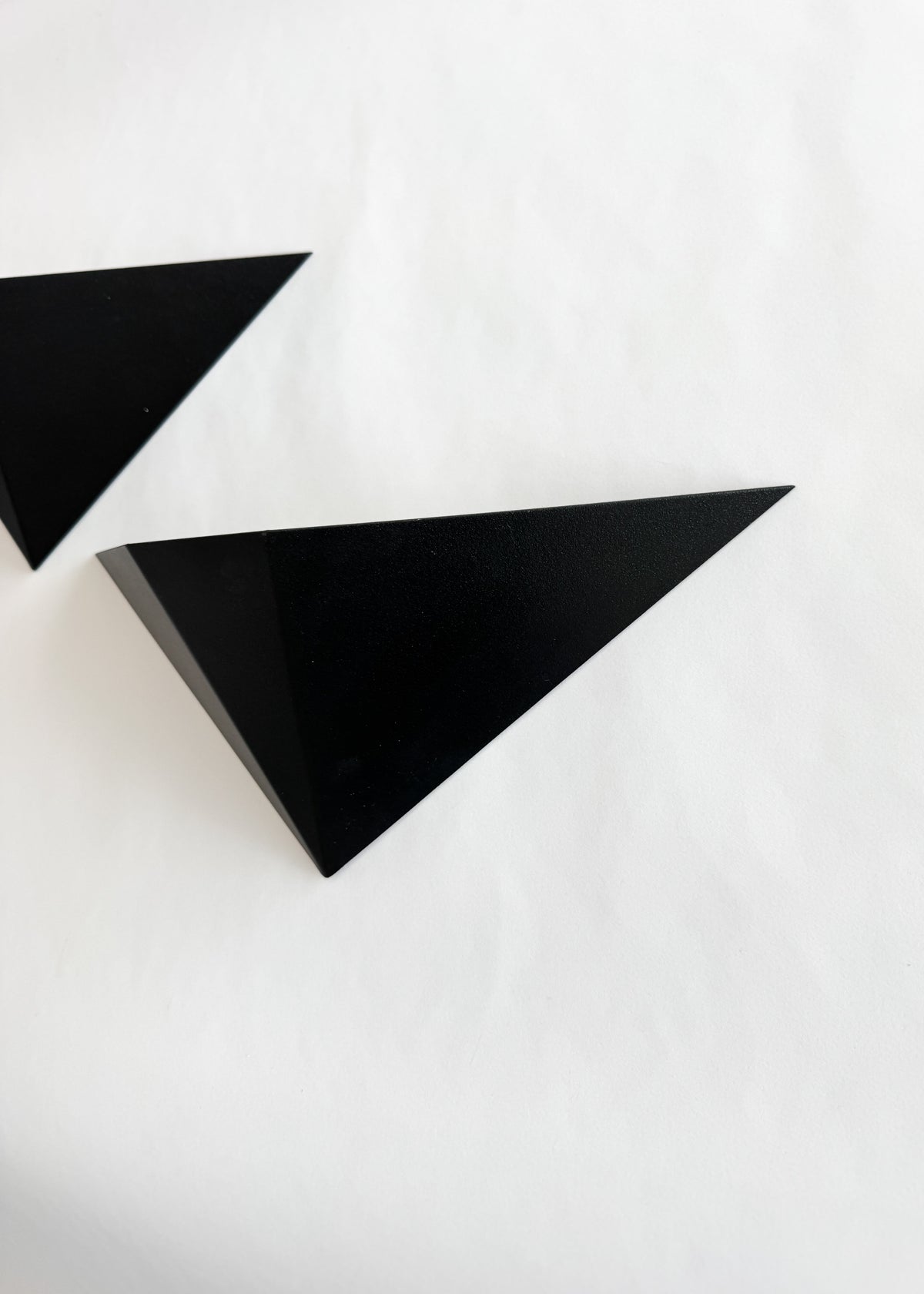 Detail of a sculptural black metal wall sconce showing its sharply defined triangular planes and light-catching finish.