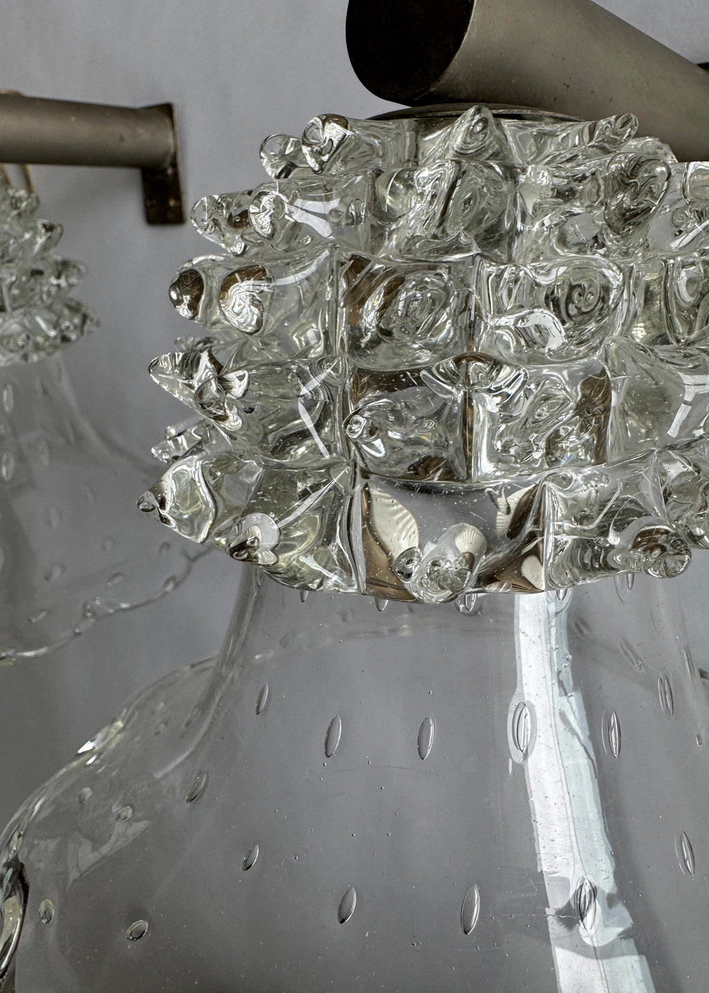 Close-up detail of a clear glass pendant light fixture with a textured, bubble-like decorative collar and a brushed metal rod visible at the top.