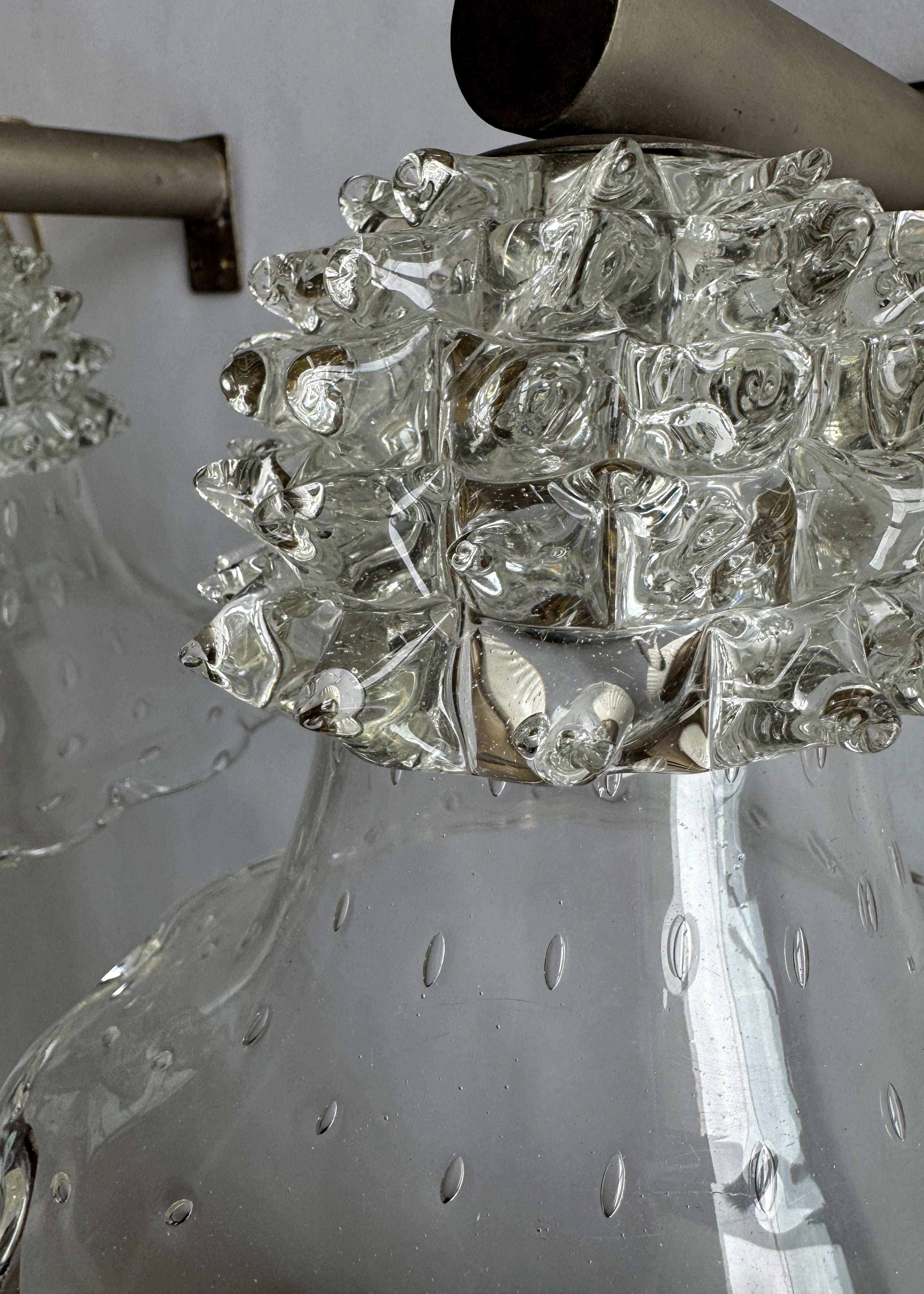 Close-up detail of a clear glass pendant light fixture with a textured, bubble-like decorative collar and a brushed metal rod visible at the top.