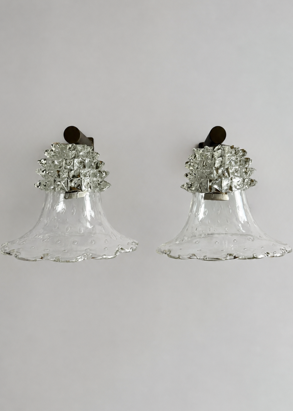 A pair of vintage bell-shaped wall sconces made of clear textured glass with silver-toned metal floral accents and dark wall mounts, shown against a plain light gray background.