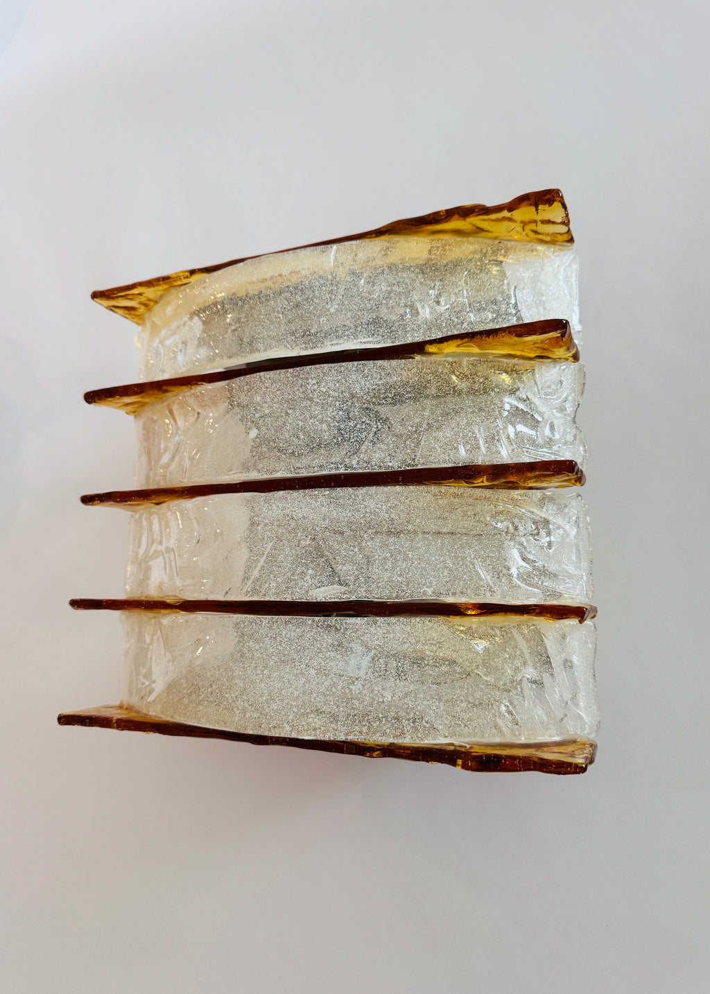 A vintage-style rectangular wall sconce featuring four stacked tiers of textured, crackled clear glass with warm amber-brown metallic trim, shown against a plain light gray background.