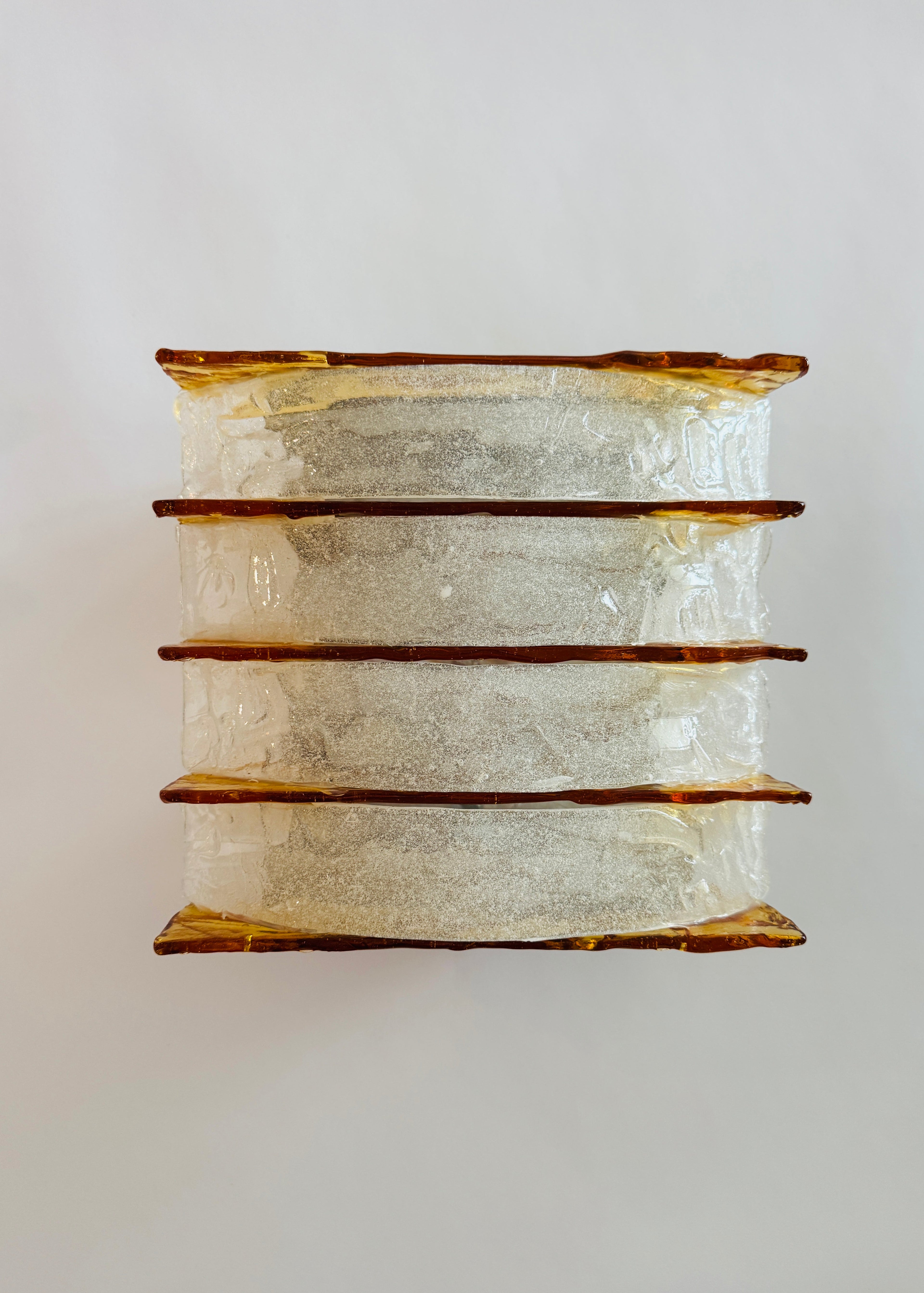 A vintage-style rectangular wall sconce featuring four stacked tiers of textured, crackled clear glass with warm amber-brown metallic trim, shown against a plain light gray background.