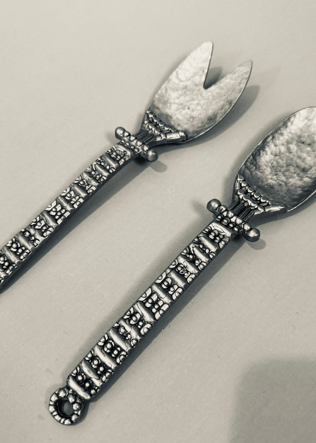 Vintage pewter salad serving set with decorative handles, including fork and spoon, styled on a neutral background