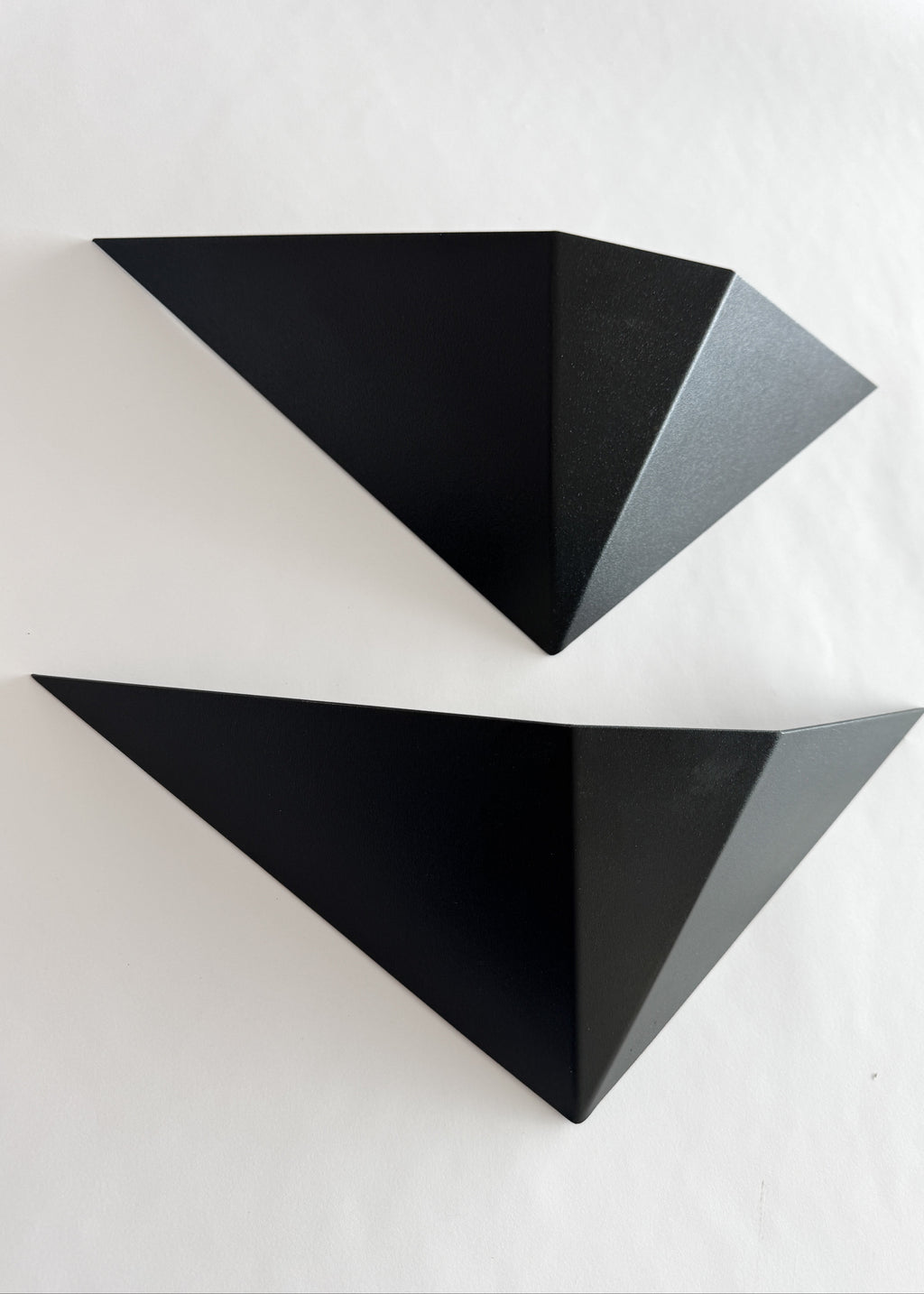 Close-up of the faceted black metal surface of a geometric wall sconce, highlighting its angular planes and textured finish.