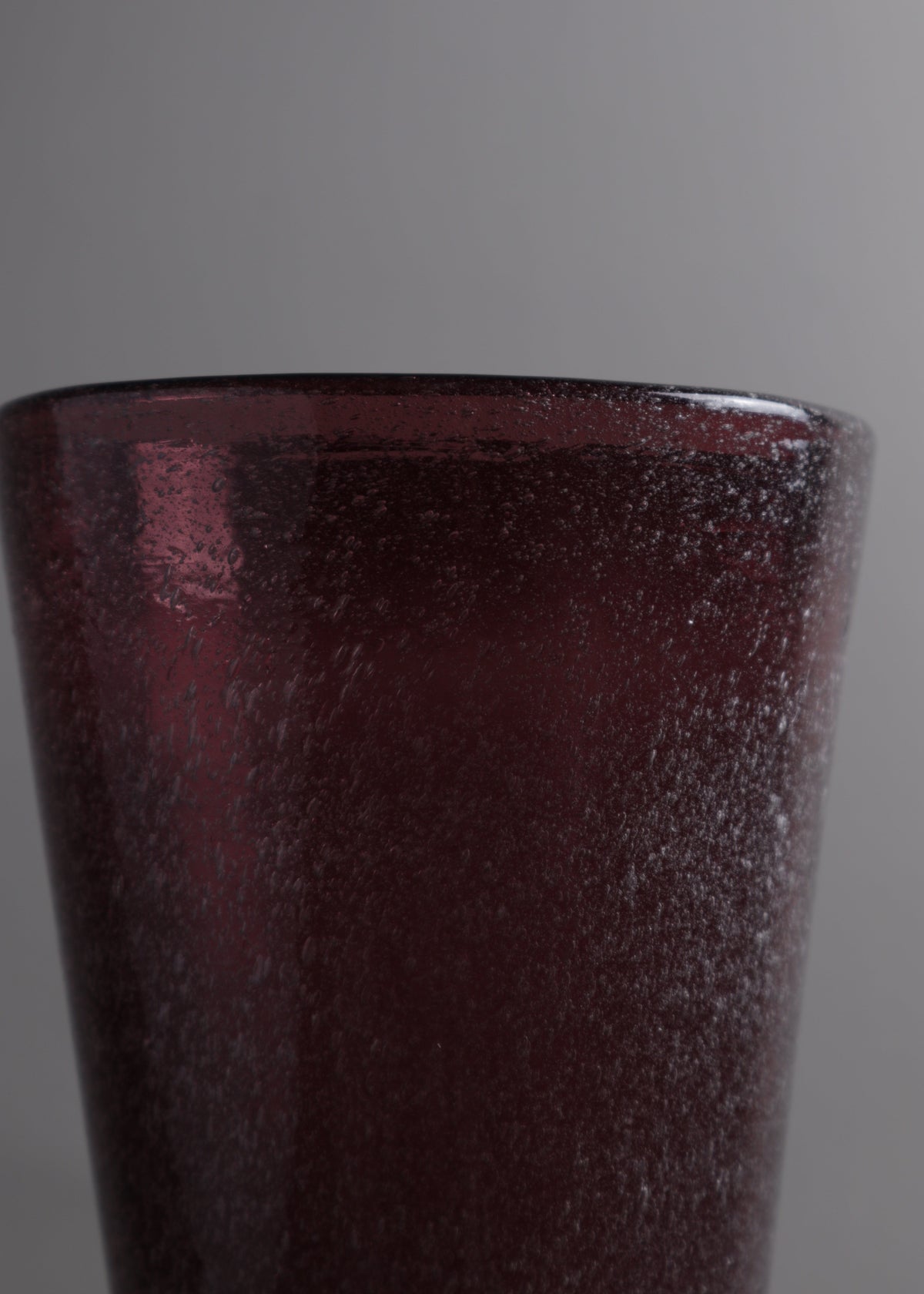 Close-up of the rim and densely bubbled plum glass surface of the Italian vase.
