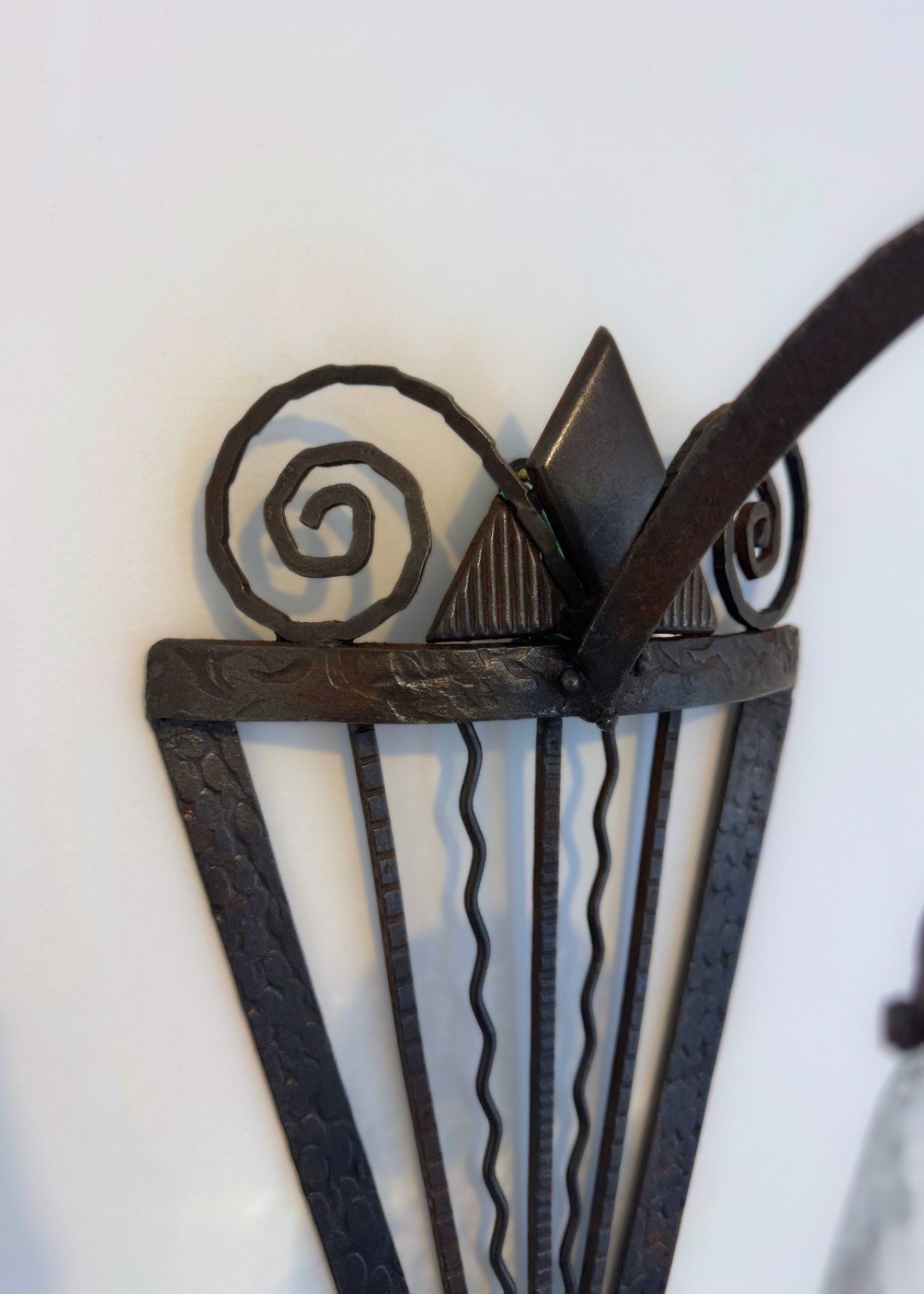 Close-up of the sculptural forged-iron wall bracket with spiral scrollwork, triangular forms and textured metal.