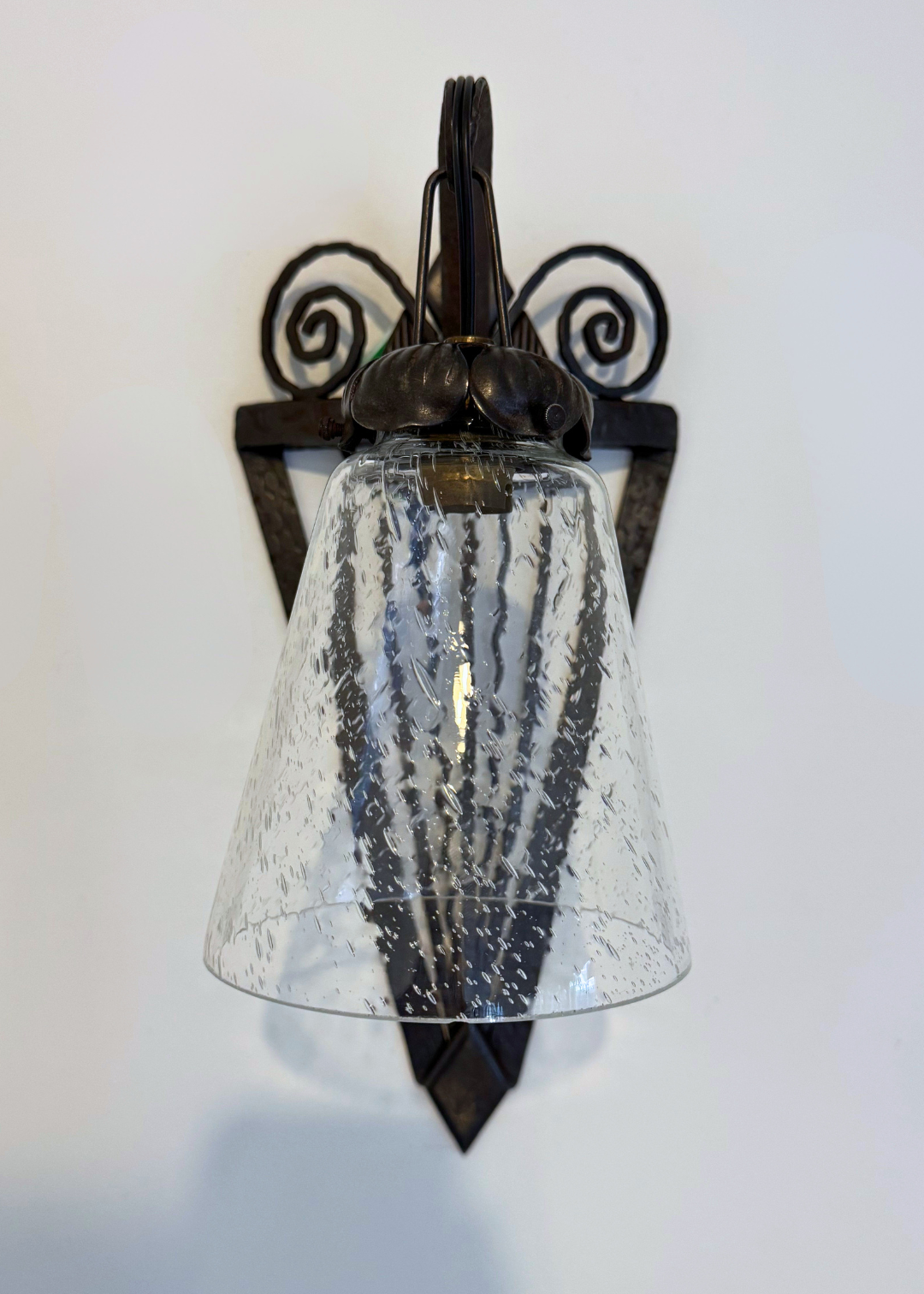Close-up of a French Art Deco wall sconce showing its textured glass shade and decorative forged-iron frame.