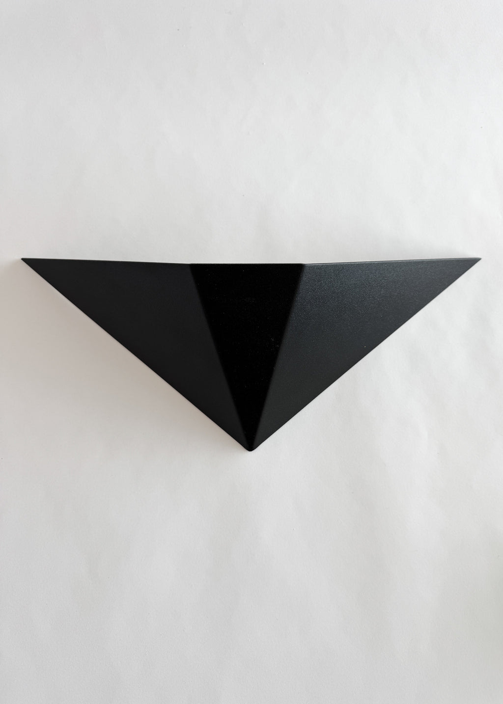 Front view of a Memphis-style black metal wall sconce with a wide triangular silhouette and pointed lower edge.