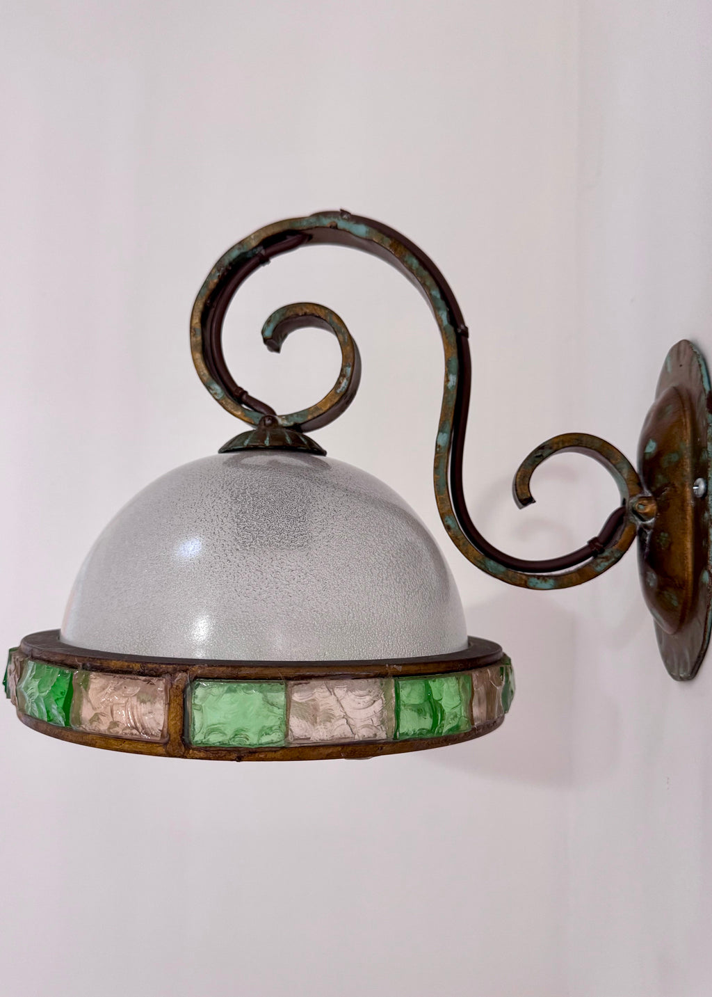Close view of a vintage Italian wall light showing its curled brass arm, patinated finish and frosted glass dome.
