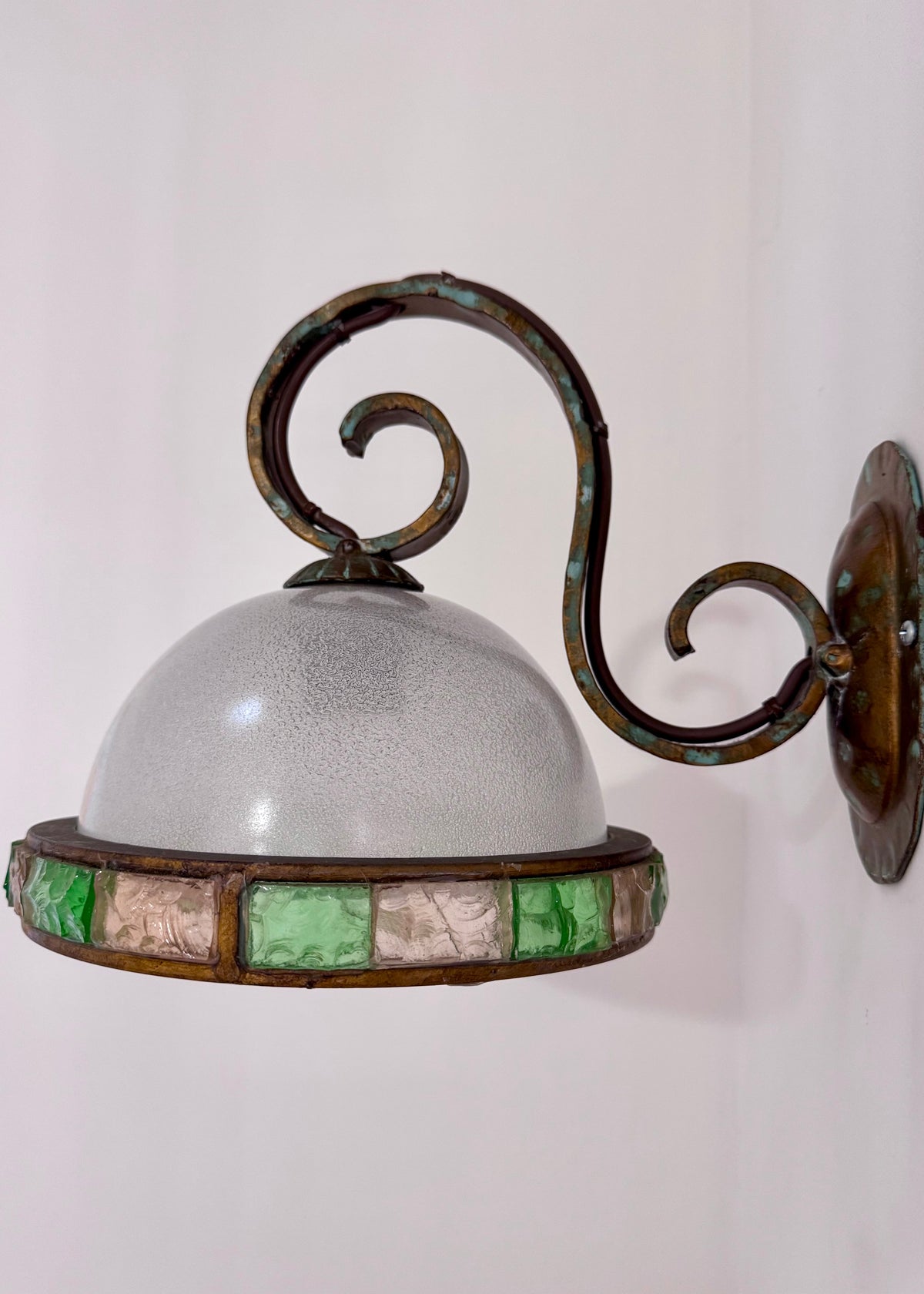 Close view of a vintage Italian wall light showing its curled brass arm, patinated finish and frosted glass dome.