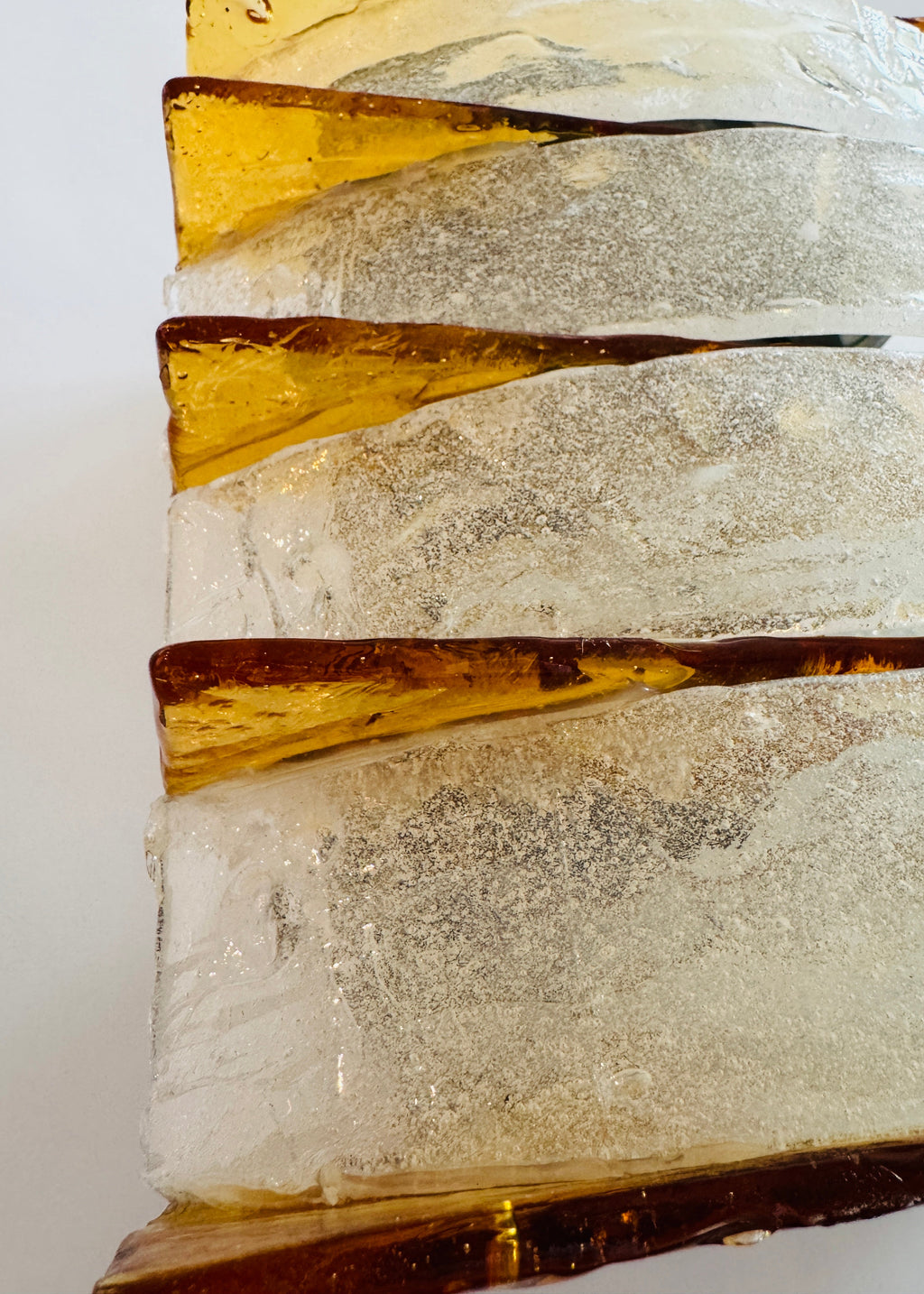 A vintage-style rectangular wall sconce featuring four stacked tiers of textured, crackled clear glass with warm amber-brown metallic trim, shown against a plain light gray background.