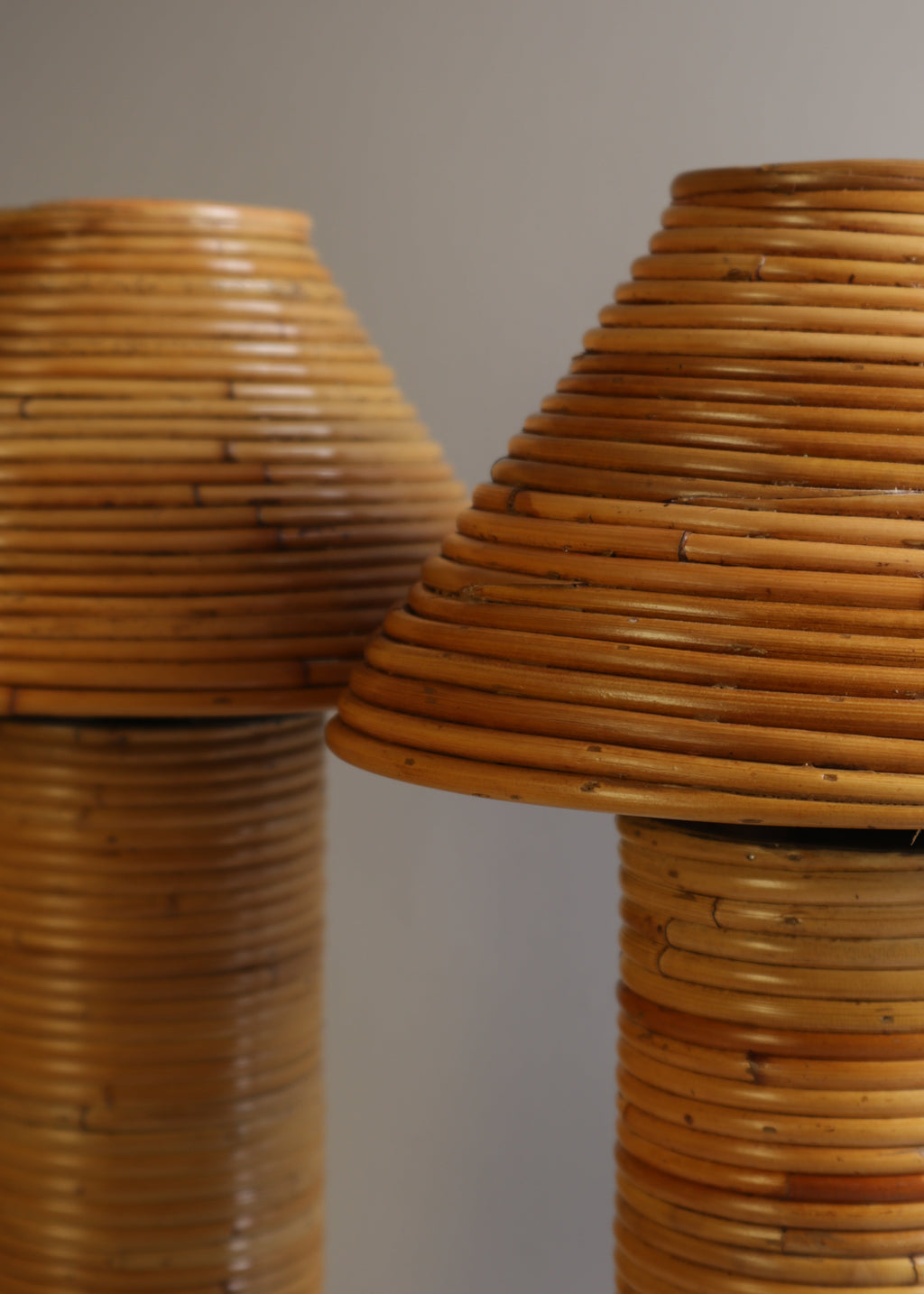 Close-up of two woven rattan or wicker lamp shades in warm tan and brown tones against a plain light gray background.