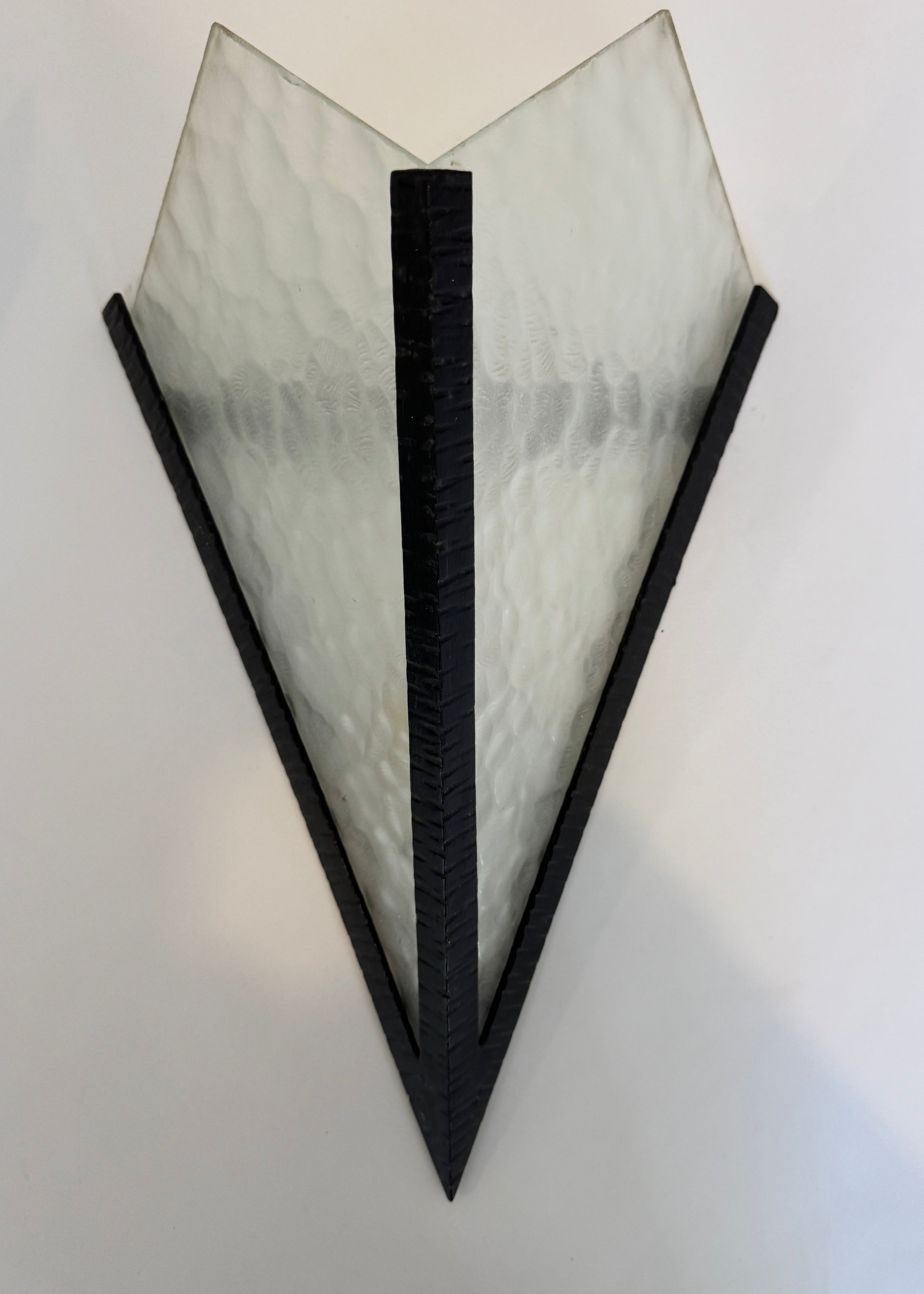 Triangular wall sconce with black frame and textured glass shade on a white background