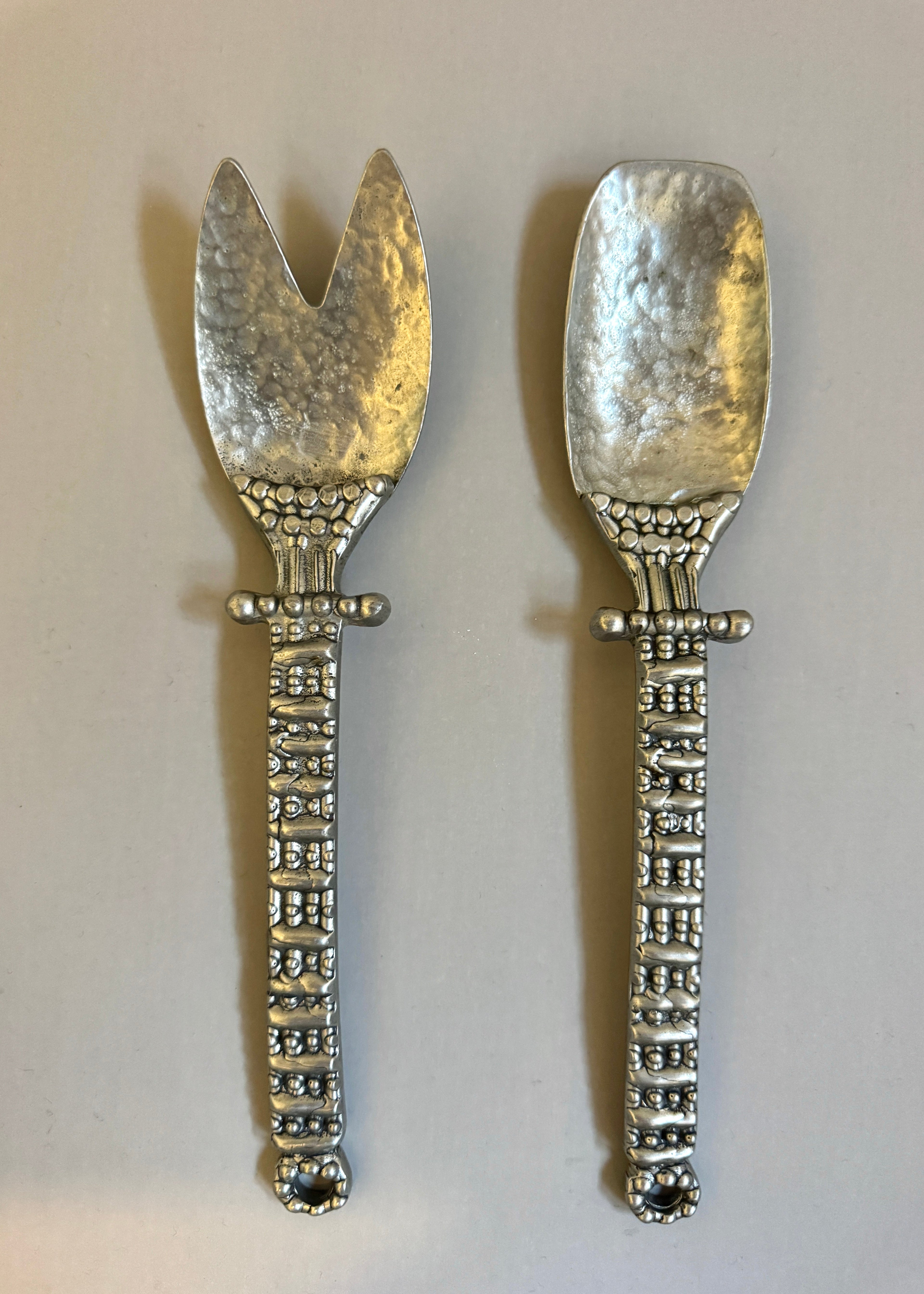 Vintage pewter salad serving set with decorative handles, including fork and spoon, styled on a neutral background