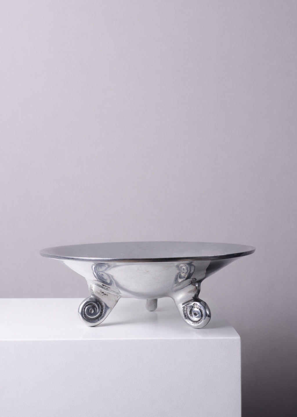 Vintage silver trinket bowl with sculptural scroll feet displayed on a white plinth